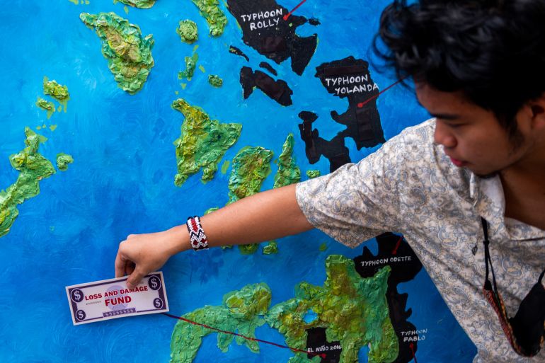 A climate activist demanding reparations puts a mock-up money bill on a Philippine map showing the areas most impacted by recent climate disasters, at a protest in Makati City, Metro Manila, Philippines, on February 28, 2023. [Reuters/Lisa Marie David]