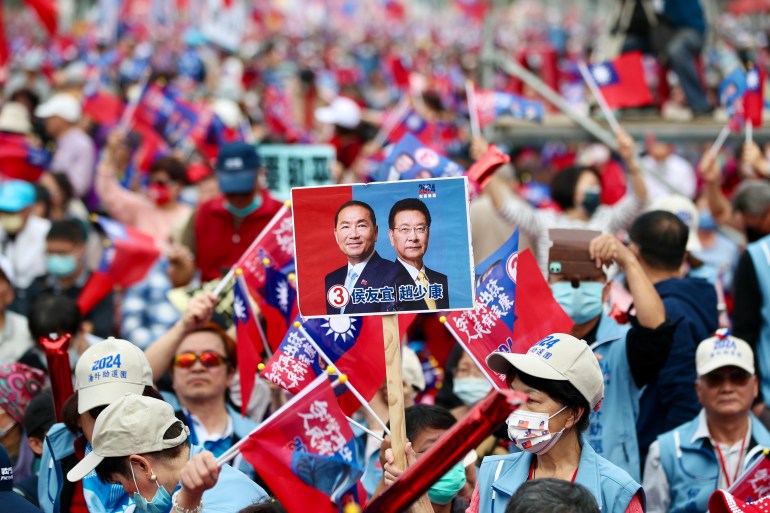 Uma multidão de pessoas em um comício do KMT.  Eles agitam bandeiras e seguram cartazes com seus candidatos.