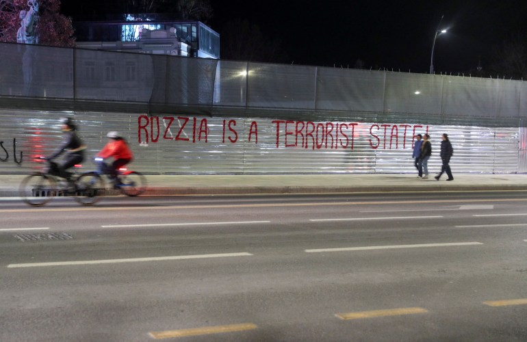Menschen bewegen sich an einem antirussischen Graffiti vorbei, das auf eine Baubarriere in einer Straße in Tiflis, Georgien, gemalt ist, 15. Februar 2023. REUTERS/Irakli Gedenidze