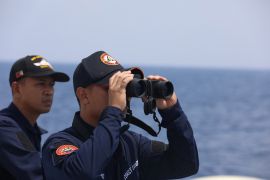 A Philippine Coast Guard personnel looks through a binocular while conducting a resupply mission for Filipino troops stationed at a grounded warship in the South China Sea,