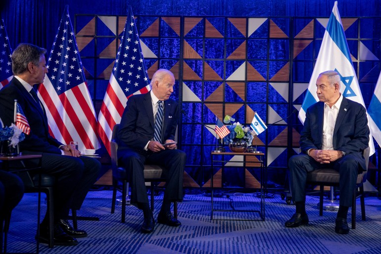 Joe Biden and Benjamin Netanyahu sit on a blue stage, next to a cluster of flags representing the US and Israel.