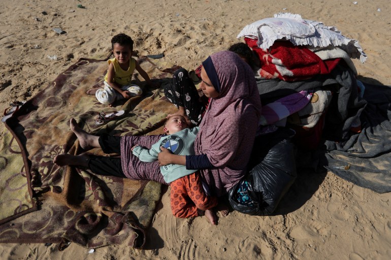 A woman sits with children outside, as displaced Palestinians, who fled their houses due to Israeli strike, shelter in a camp in Rafah