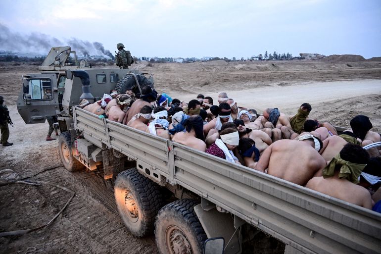 Soldati israeliani stanno accanto a un camion pieno di detenuti palestinesi a torso nudo