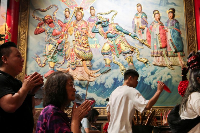 People pray to the sea goddess Mazu. There is a large mural of her on the wall behind them