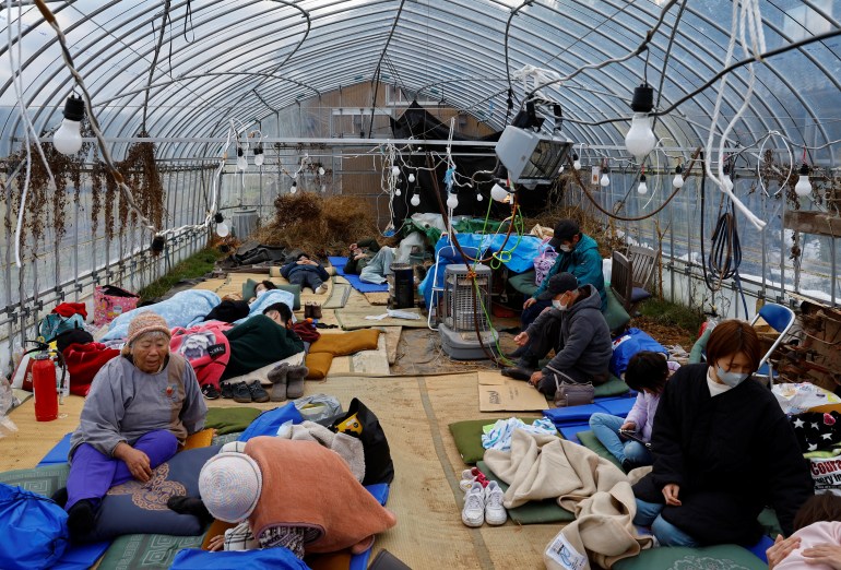 People taking shelter in a green house after the quake. They are sitting on the floor. They are wearing winter clothes and some have blankets around them