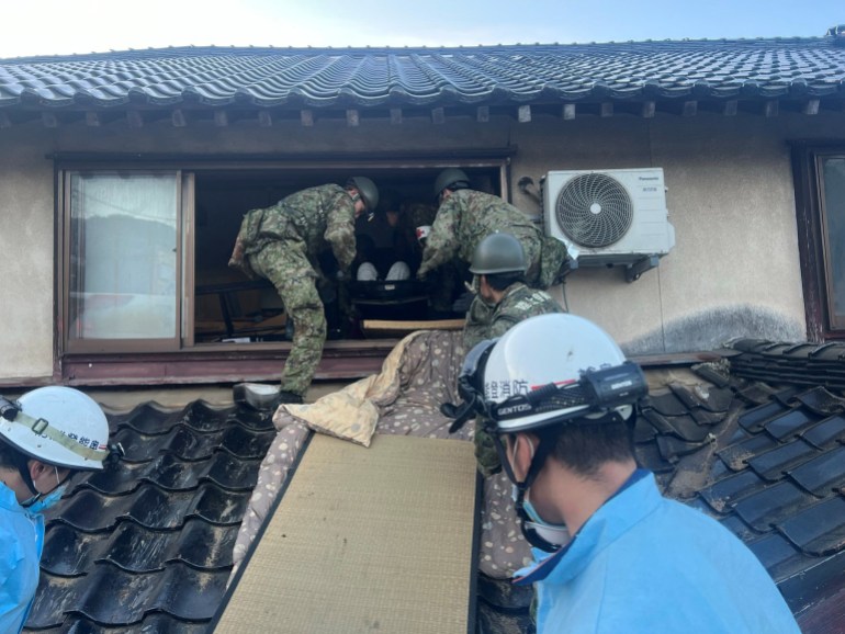 Dos soldados japoneses intentan sacar a alguien del piso superior de su casa en ruinas. 