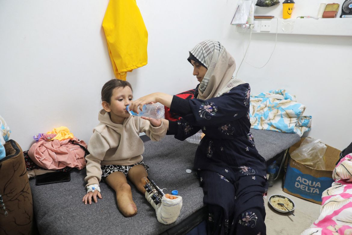 Palestinian girl Eman Al-Kholi, whose limb was amputated after being wounded in an Israeli strike that killed her parents, is helped to drink water by a relative as she receives treatment at the European Hospital, in Rafah in the southern Gaza Strip