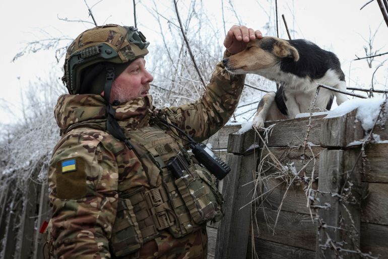 A Ukrainian soldier in a trench on the front line petting a dog