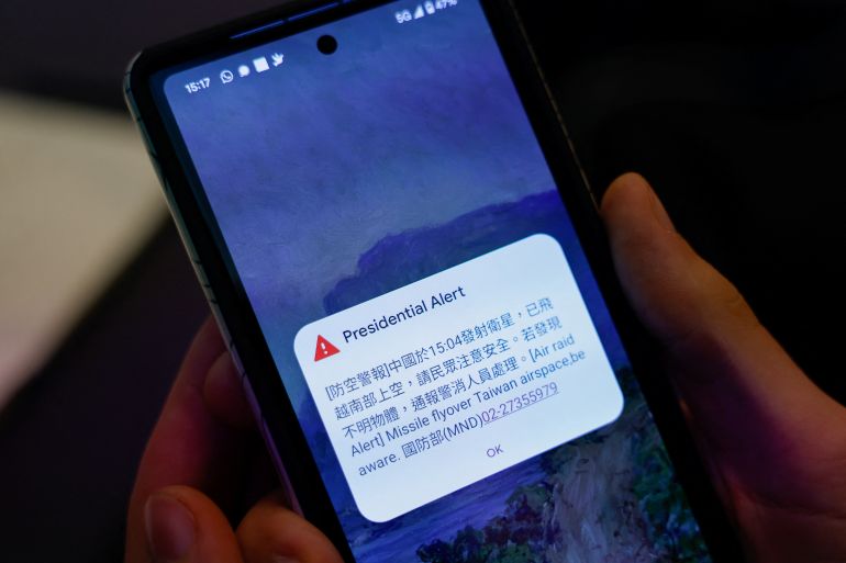 A person attending a Foreign Ministry's news conference holds a phone showing air raid alert about a Chinese satellite that had flown over south Taiwan airspace in Taipei