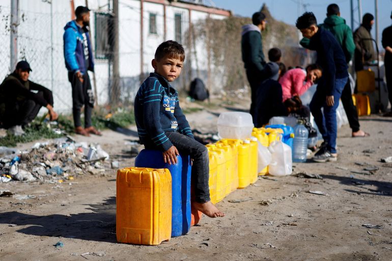A displaced Palestinian boy, who fled his house due to Israeli strikes, sits on a water canister at a tent camp
