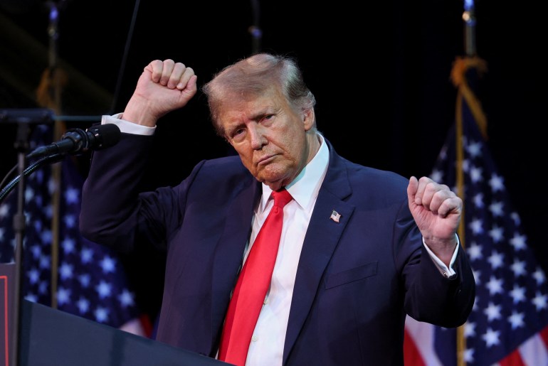 Donald Trump agitando as mãos no ar em um comício de campanha