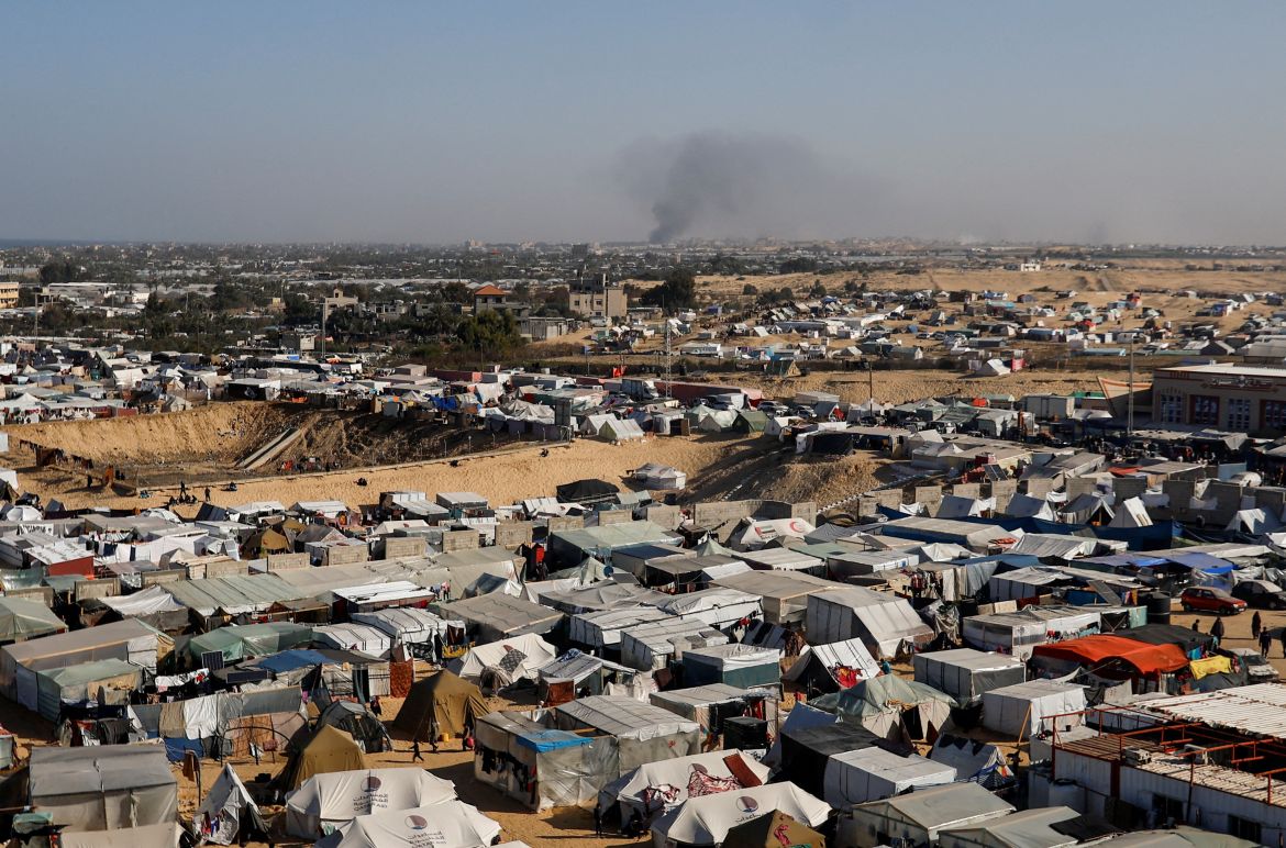 A general view of a tent camp housing displaced Palestinians, as smoke rises in the distance due to an Israeli ground operation in Khan Younis