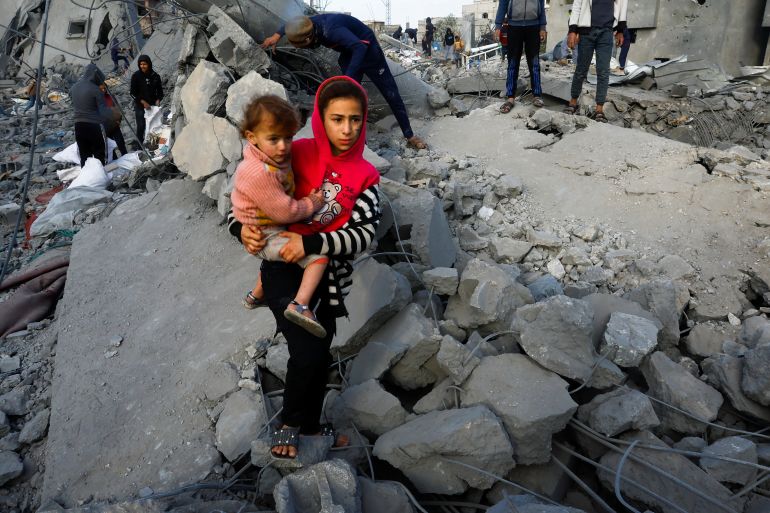A Palestinian girl carrying a child amid rubble in Gaza