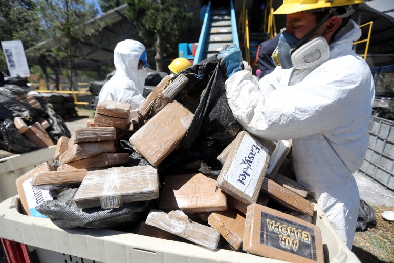 Authorities dressed in protective white coveralls and masks designed to filter the air they breath empty garbage bags filled with cardboard packages, allegedly containing drugs.