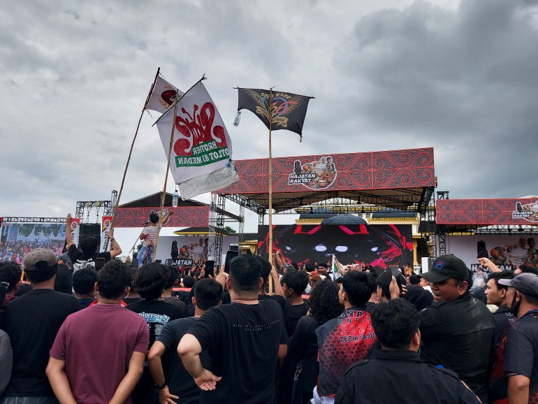 Slank fans waving flags with the band’s logos on them. The fans are mostly wearing black.