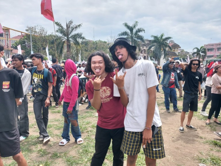 University student Mulia with a friend. He is wearing a whit T-shirt and brown checked shorts. They are posing and sticking out their tongues