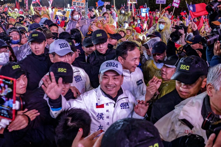 Kuomintang (KMT) presidential candidate Hou Yu-ih shakes hands with his supporters at a campaign rally.  He is extending his hand and smiling.