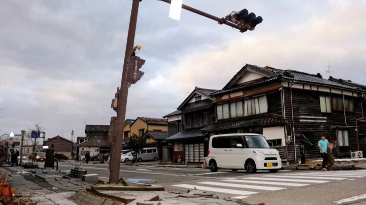 A car drives past a badly damaged pavement along a street in the city of Wajima