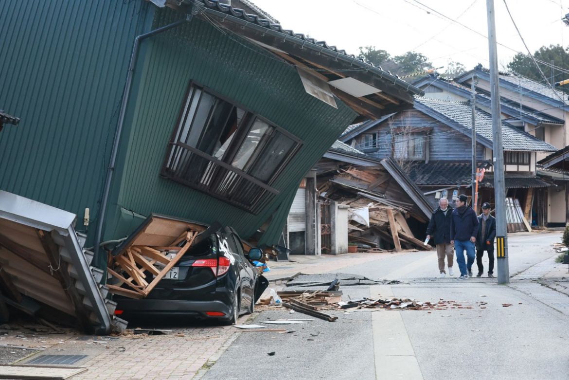 People walk past a badly damaged house in the city of Nanao, Ishikawa Prefecture.