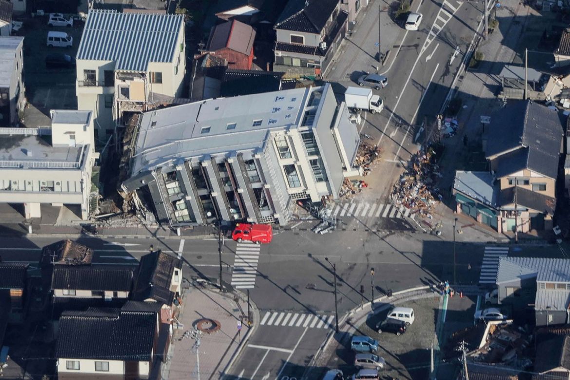 This aerial photo provided by Jiji Press shows a rescue vehicle (C) parked next to a seven-storey building which fell over in Wajima, Ishikawa prefecture.