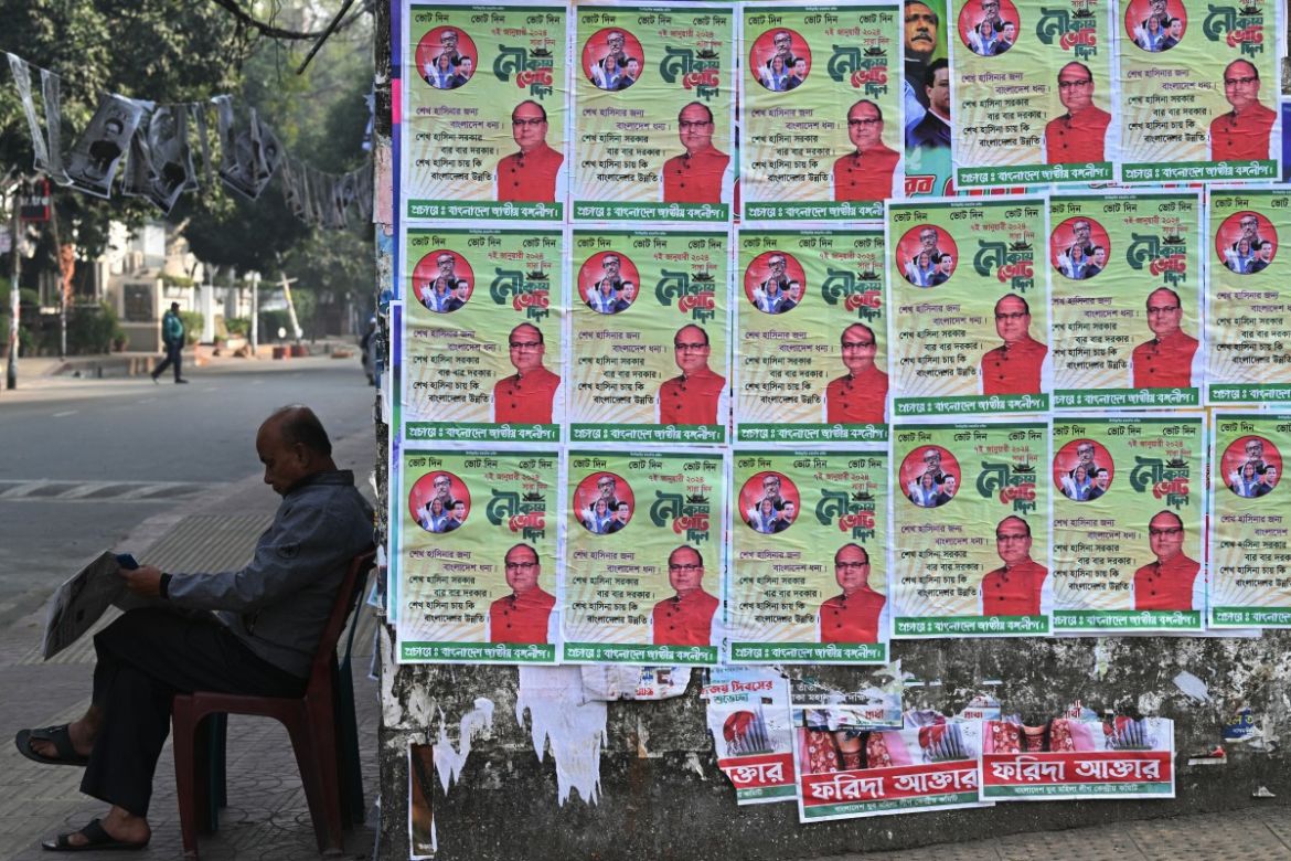 A resident reads a newspaper sitting next to election posters of Awami League party, ahead of the upcoming general elections, in Dhaka on January 5, 2024.