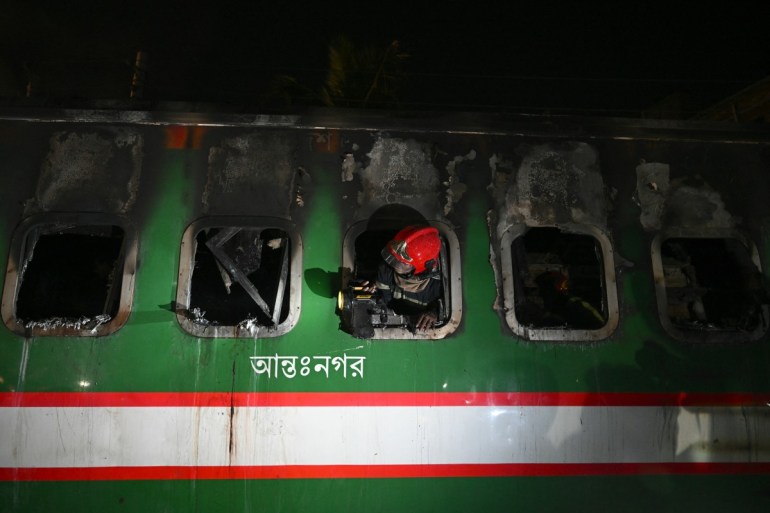 Ein bangladeschischer Retter leuchtet mit seiner Taschenlampe aus einem Fenster, während er am 5. Januar 2024 in Dhaka einen ausgebrannten Waggon des Benapole Express durchsucht