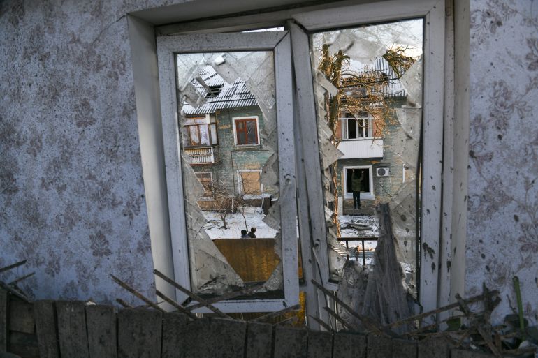 Um homem cobre uma janela danificada com um painel de fibra em um conjunto habitacional de dois andares
