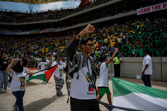 pessoas marcham em um estádio carregando bandeiras palestinas