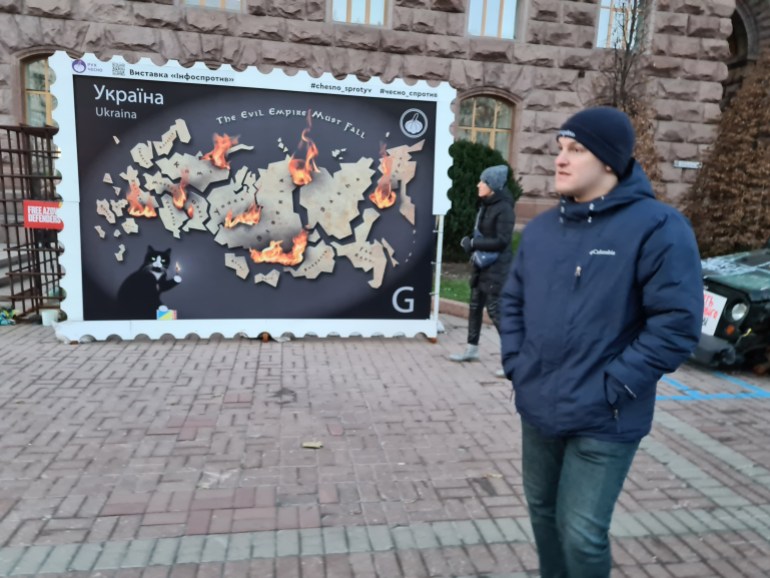 A Ukrainian walks past a mock postage stamp depicting a 'burning' Russian map with words 'The evil empire must fall'