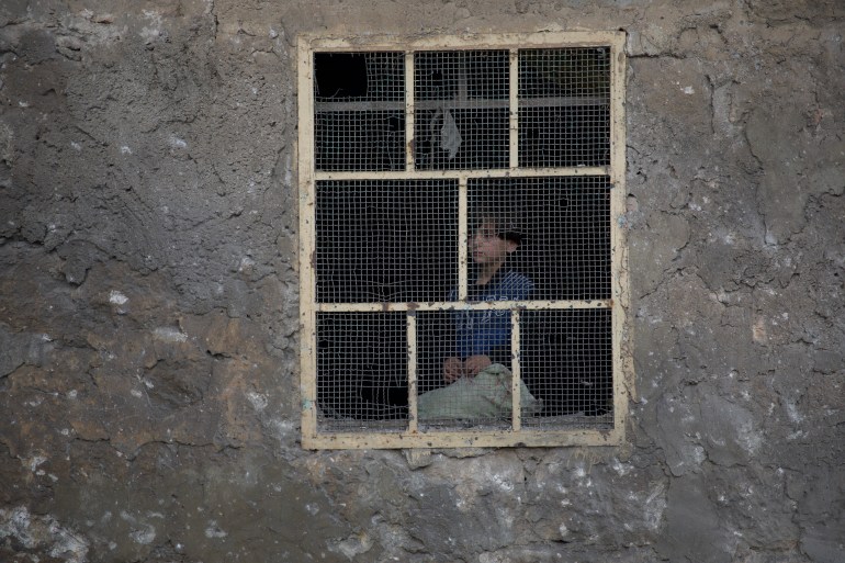Uma criança olha com cautela para a rua a partir da janela da sua casa, onde se esconde dos repetidos bombardeamentos das forças do regime em Darat Azza, na zona rural ocidental de Aleppo, no primeiro dia de 2024.