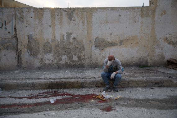 A man sitting on the sidewalk was overcome with emotion at the sight of the blood of his relative who was killed in one of the neighborhoods of Darat Azza in the western countryside of Aleppo