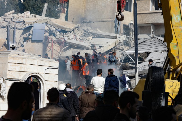 People and rescuers gather in front of a building destroyed in a reported Israeli strike in Damascus on January 20, 2024