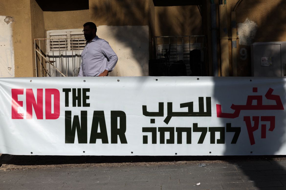 A man stands behind an anti-war banner during a protest calling for a ceasefire and for the release of Israeli hostages held in Gaza since the October 7 attack by Palestinian militants, in the northern port city of Haifa on January 20