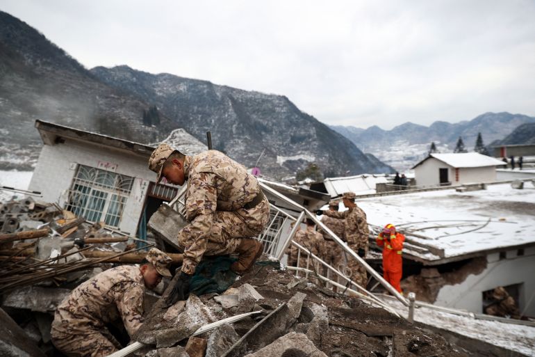 Soldiers involved in rescue efforts, Steep mountains are behind. They are dusted with snow.