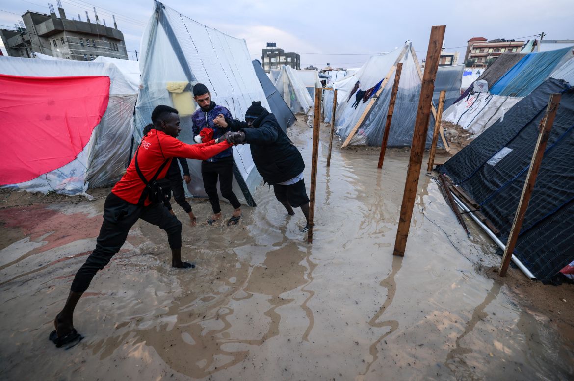 A displaced Palestinian man helps a woman to find her way amid tents flooded by heavy rain, at a makeshift camp set up by people who fled the ongoing battles between Israel and Hamas militants, in Rafah in the southern Gaza Strip on January 27