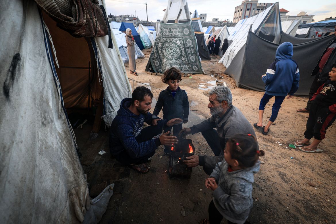 Displaced Palestinians try to warm up around a fire amid tents flooded by heavy rain, at a makeshift camp in Rafah