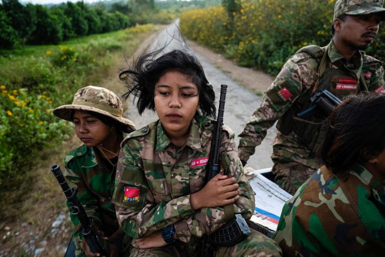 A woman fighter with the Mandalay People's Defence Force, She is travelling on the back of a truck with other fighters and is holding her weapon