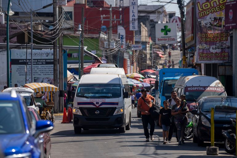A bus travels along a busy street in Tapachula, Mexico. A family walks along the roadside.