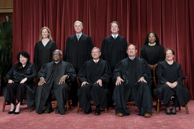 A portrait photo of all nine US Supreme Court justices, dressed in black robes and arranged in two lines, some seated, some standing.