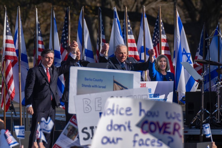 Protesters gather in Washington, DC, to see Chuck Schumer and other Congressional leaders speak at a March for Israel. The stage for the speakers is set up with US and Israeli flags, and audience members wave signs.