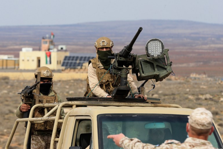 Um soldado jordaniano está na traseira de um caminhão militar, atrás de uma metralhadora montada.