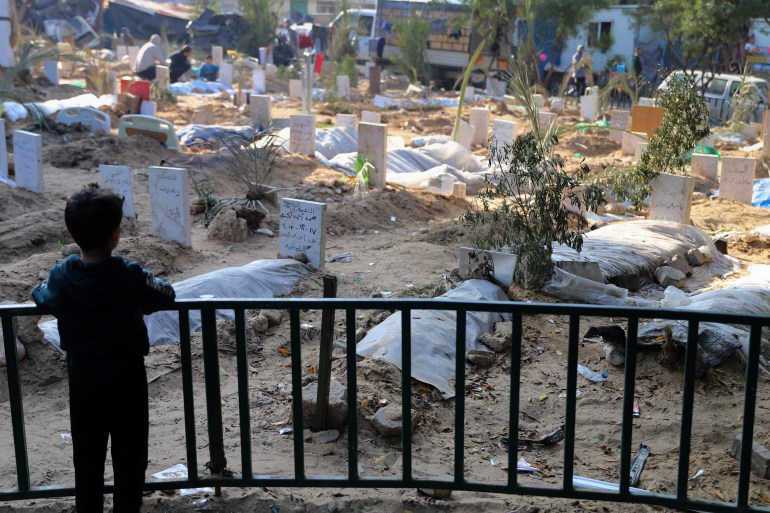 A Palestinian child looks at the graves of people killed in the Israeli bombardment of the Gaza Strip and buried inside the Shifa Hospital grounds in Gaza City, Sunday, Dec. 31, 2023. (AP Photo/Mohammed Hajjar)