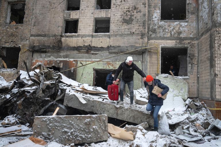 İnsanlar Salı günkü Rus saldırısından sonra yıkılan bir apartmanın eşyalarıyla yürüyor, Kiev, Ukrayna, 3 Ocak 2024