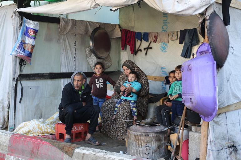 a family with children sit inside a tent in a refugee camp
