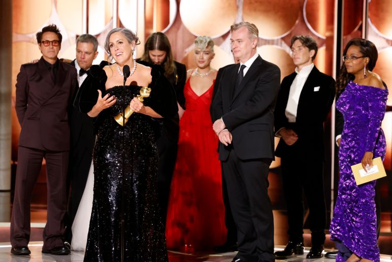 This image released by CBS shows producer Emma Thomas, foreground left, accepting the award for best motion picture drama for "Oppenheimer" as cast and crew members, background from left, Robert Downey Jr., Matt Damon, composer Ludwig Göransson, Florence Pugh, director Christopher Nolan, actor Cillian Murphy and presenter Oprah Winfrey look on during the 81st Annual Golden Globe Awards