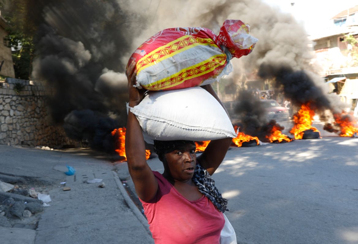 A woman walks past burning tires set on fire by protesters to call attention to the country's insecurity and demanding the resignation of the prime minister, in Port-au-Prince, Haiti, Thursday, Jan. 18