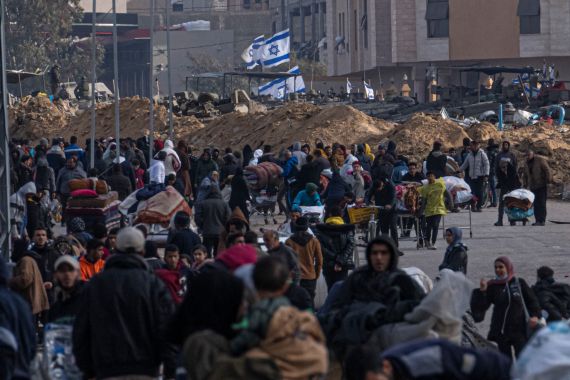 a crowd of displaced people walk past a mound with Israeli flags