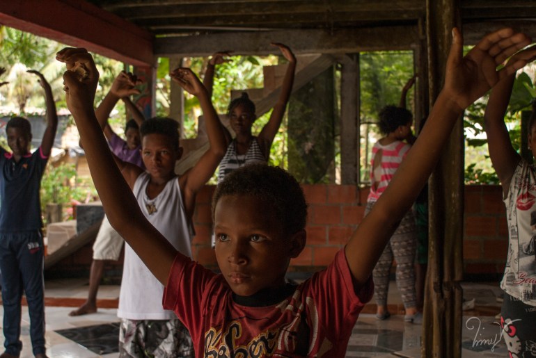 A group of children raise both arms in the air, as they practice salsa dancing in Buenaventura, Colombia.