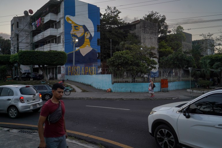 Um mural de Nayib Bukele contra uma bandeira salvadorenha é visto na lateral de um prédio perto de uma rua.