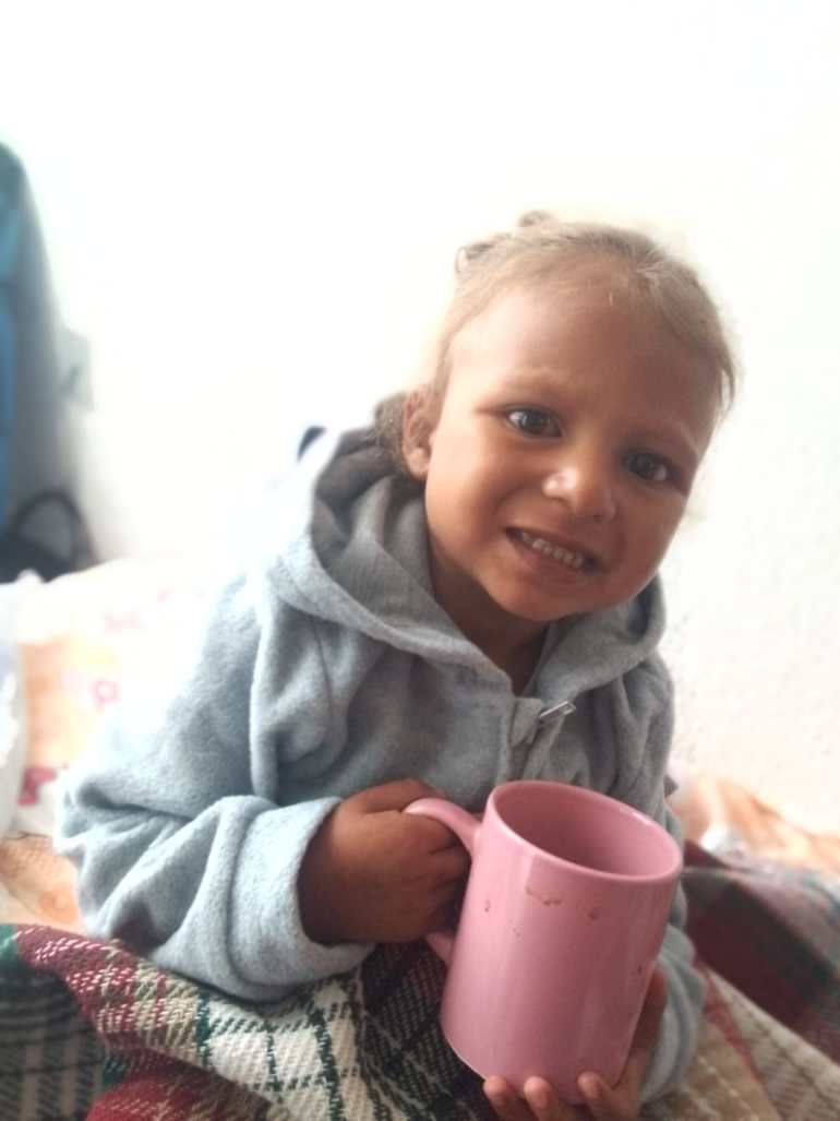 Emiliannys holds a pink mug. She wears a grey hoodie sweater and smiles.